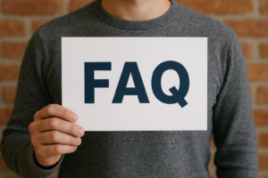 Osoba trzymająca tabliczkę z napisem „FAQ” na tle ceglanej ściany, symbolizująca sekcję najczęściej zadawanych pytań na stronie internetowej.